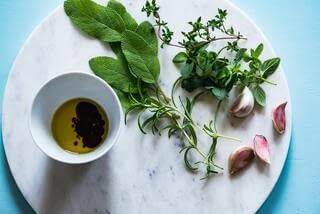 Some oil in a bowl with two kinds of leaves and garlic is on the plate