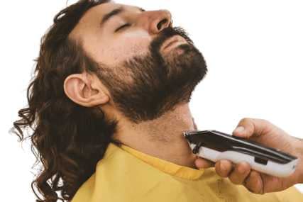 A man with a beard using electric shaver on his neck