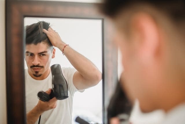 A man using a blow dryer on his hair in front of a mirror