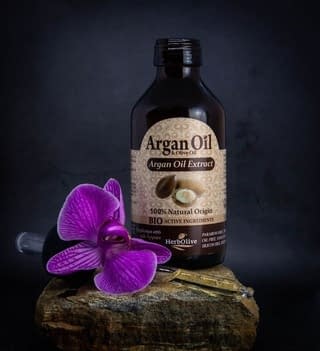 A bottle of argan oil for beard growth with violet flower placed on a stone